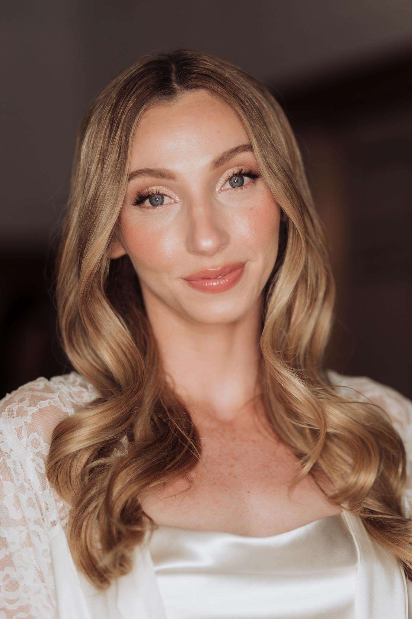 Close-up of bride in white satin slip and lace robe with champagne eyeshadow and updo