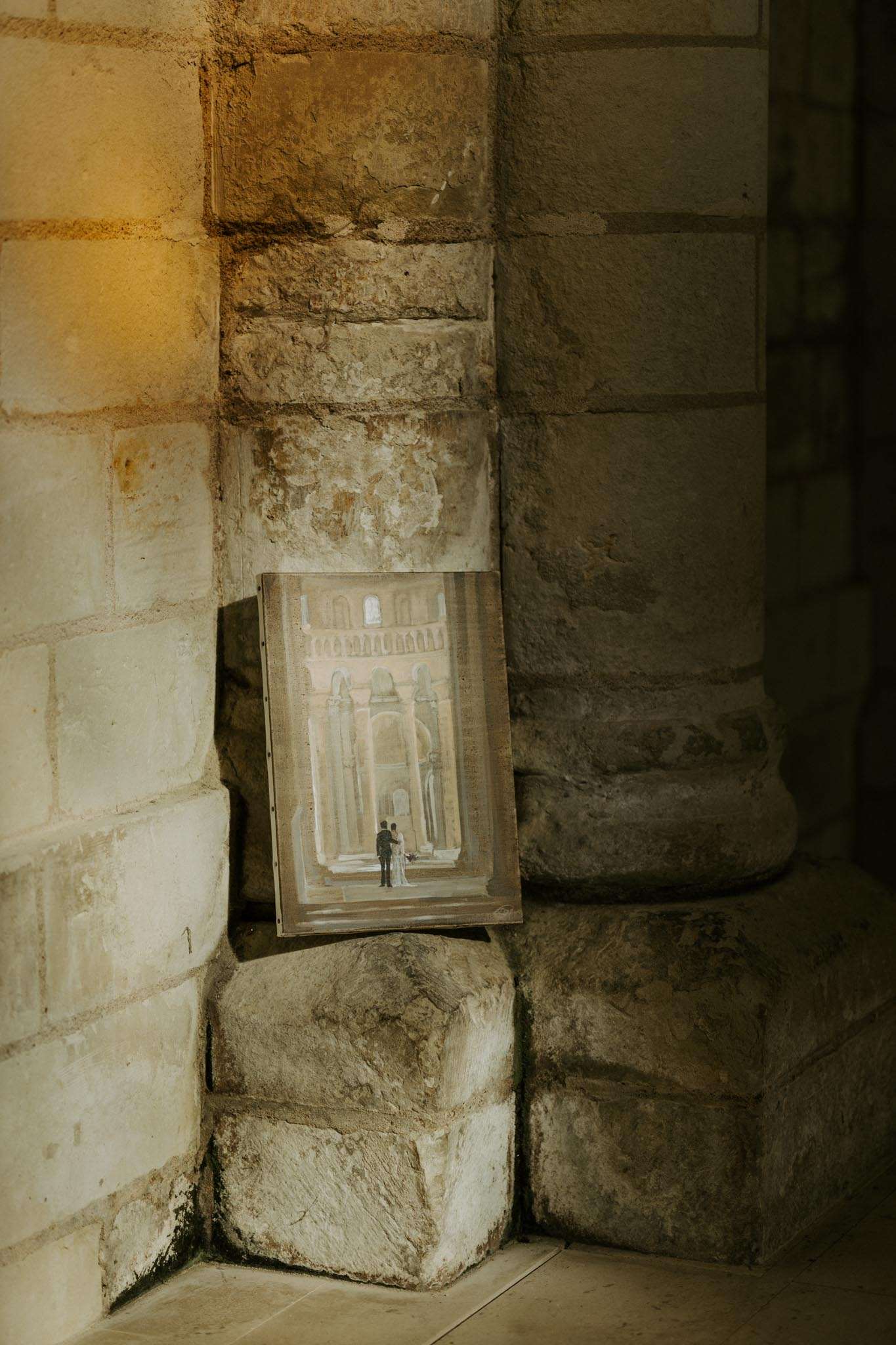 Custom wedding painting of couple under stone arches propped against limestone pillar lit by amber wall light
