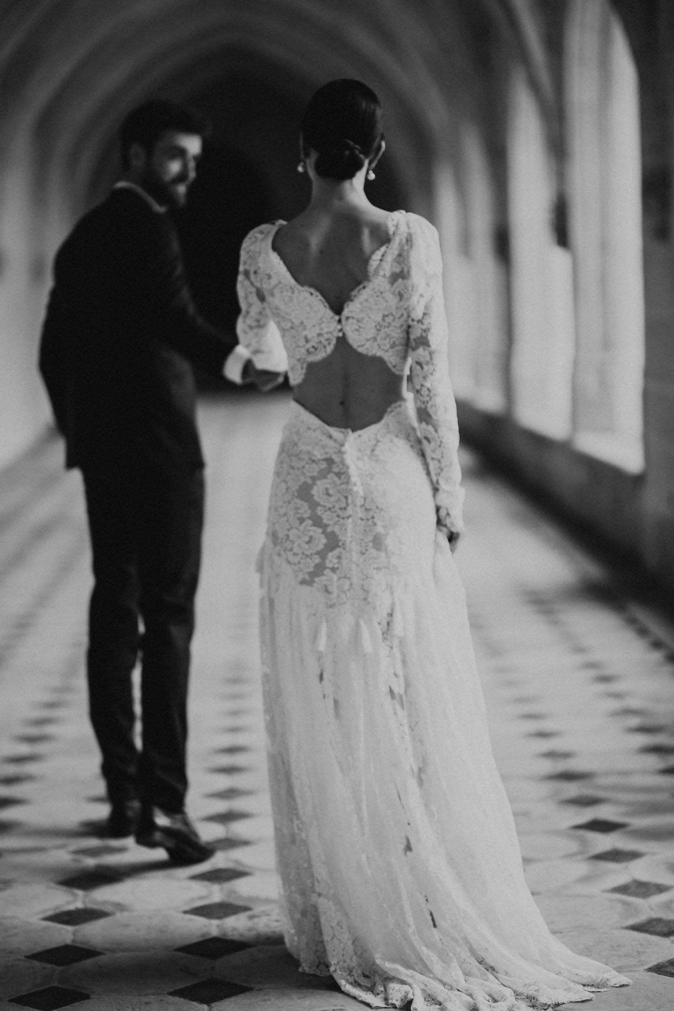 Black-and-white portrait of bride in open-back lace gown and groom in vaulted stone abbey corridor with tiled floor