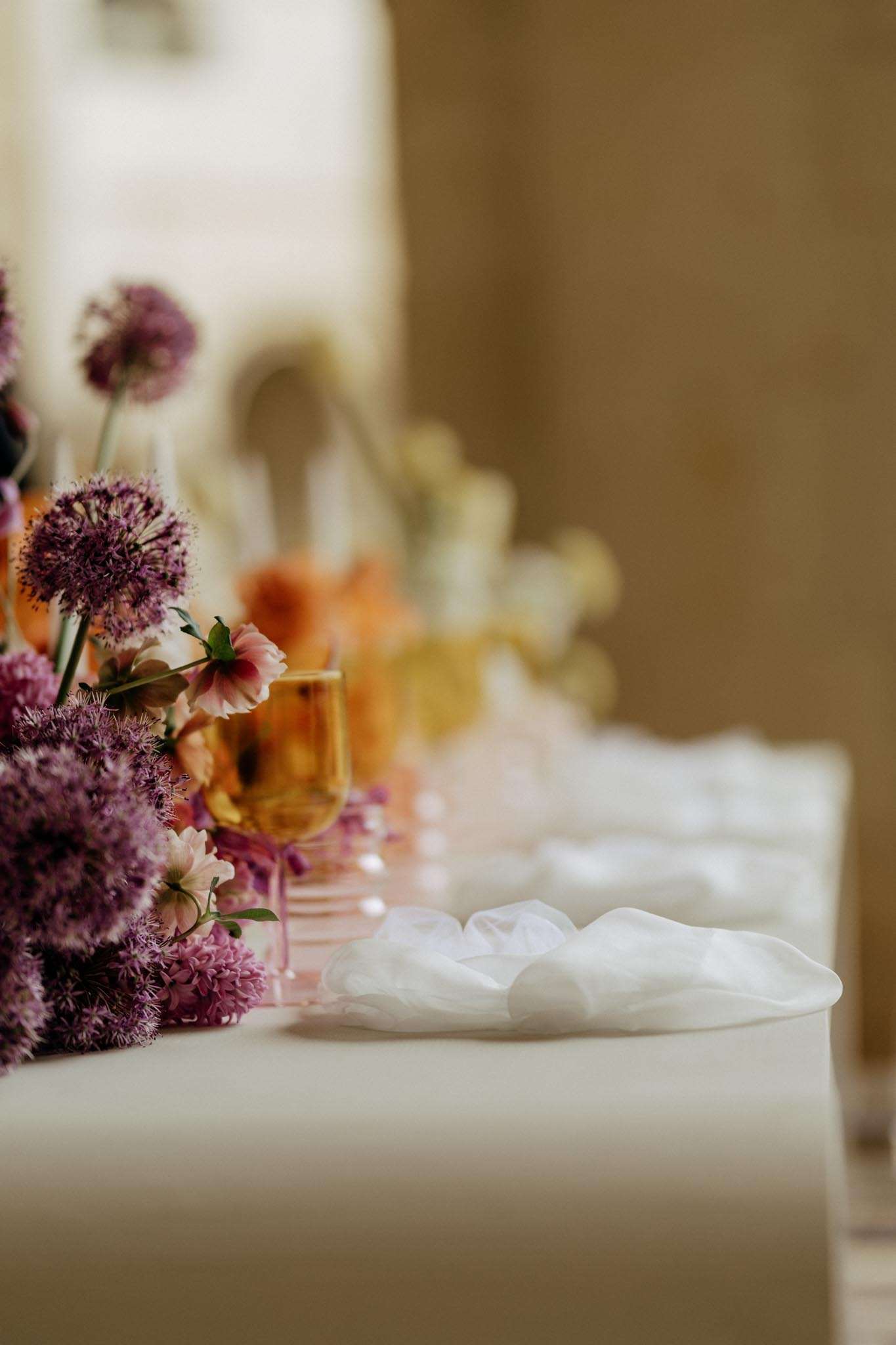 Reception table with purple allium, blush daisy, and orange floral runner with colored glassware