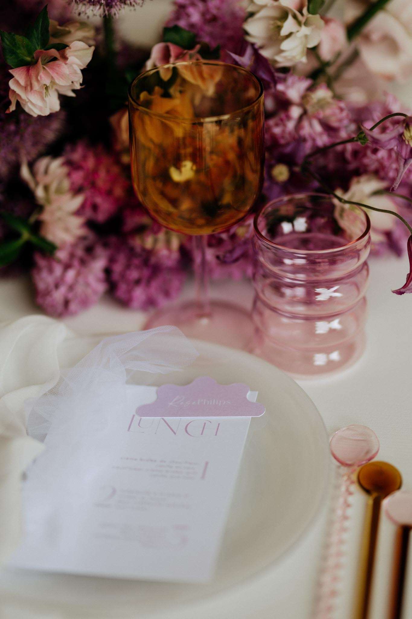 Place setting with mauve menu card, amber and pink glassware, and peony centerpiece in jewel tones