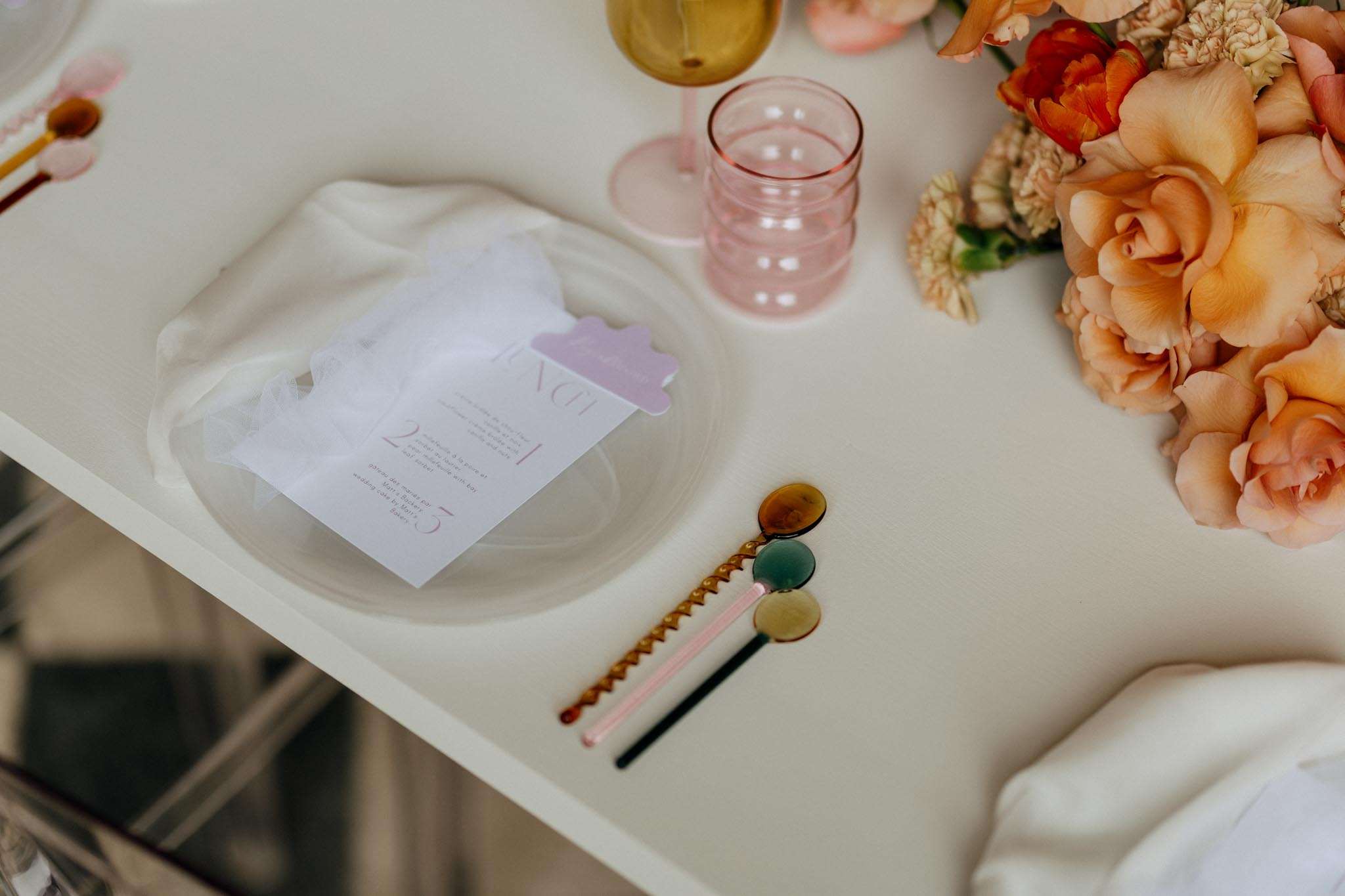 Wavy plate with illustrated menu card, ribbed pink tumbler, amber wine glass, and peach rose arrangement