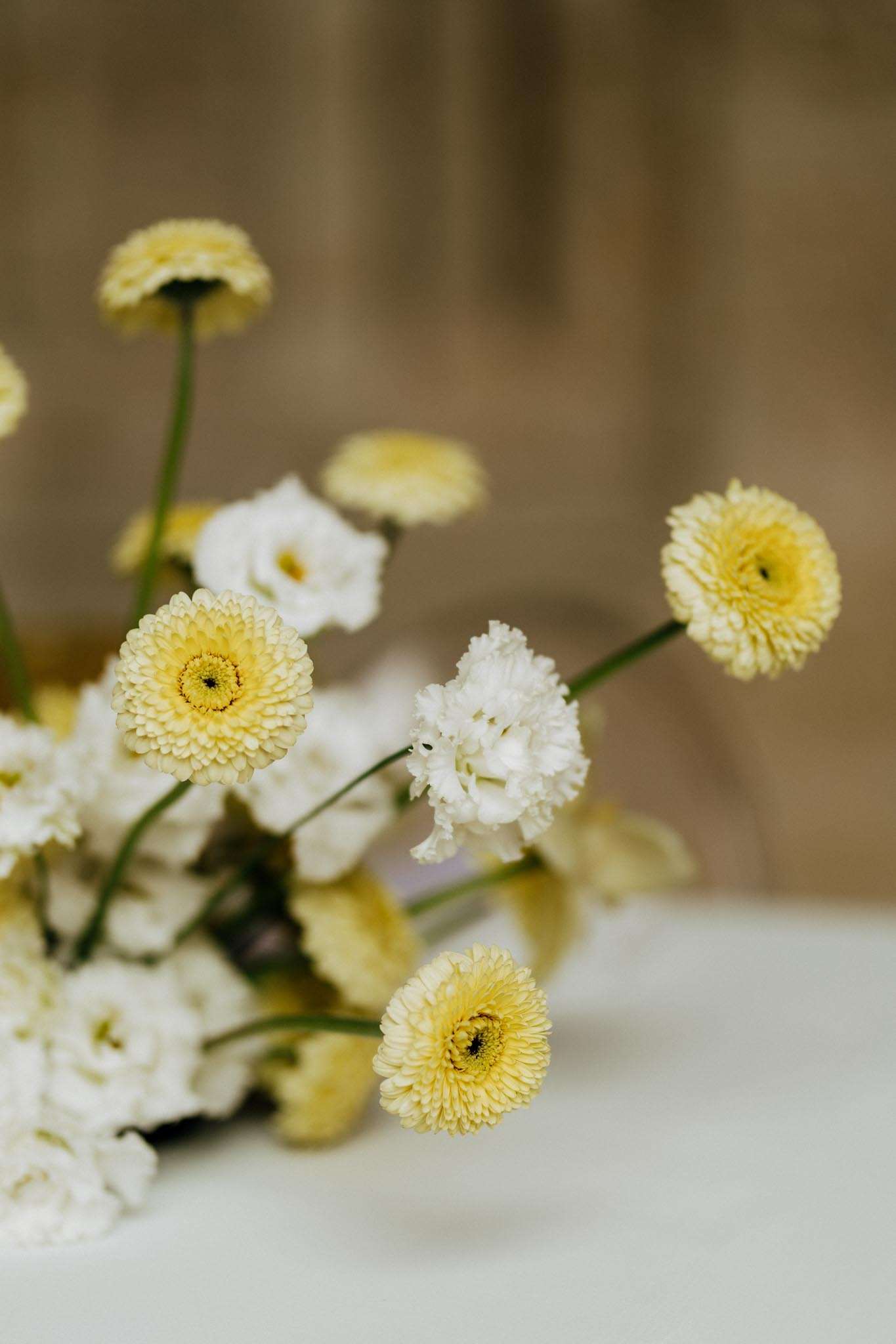 Close-up of pale yellow chrysanthemums and white lisianthus floral arrangement on white surface