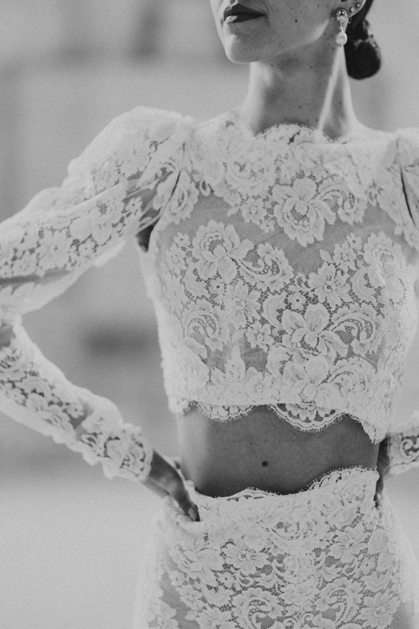 Black and white close-up of two-piece bridal lace crop top and skirt showing floral lace texture and drop earrings