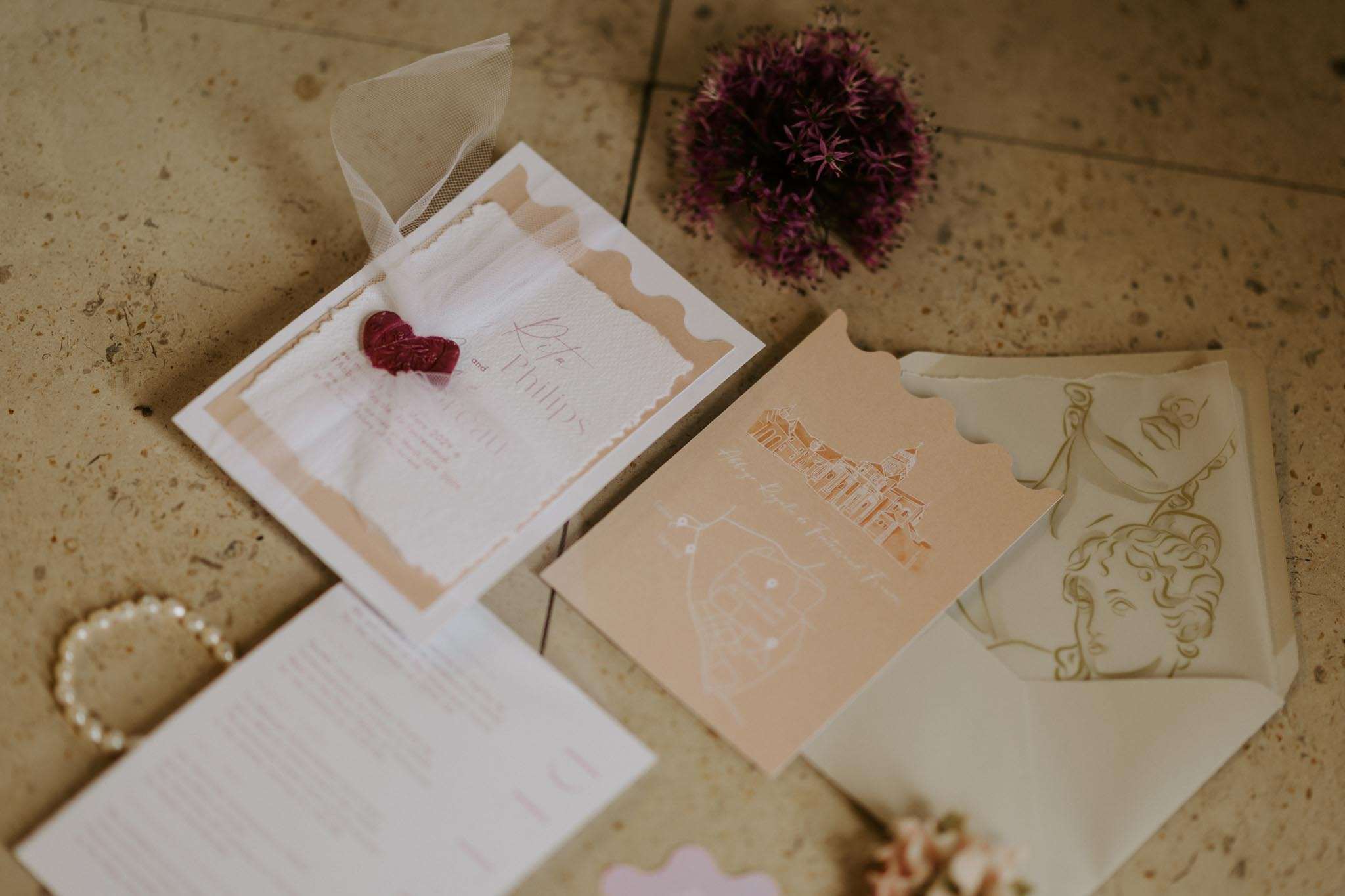Stationery flat lay with deckled invitation, red wax seal, chateau illustration, and pearl bracelet