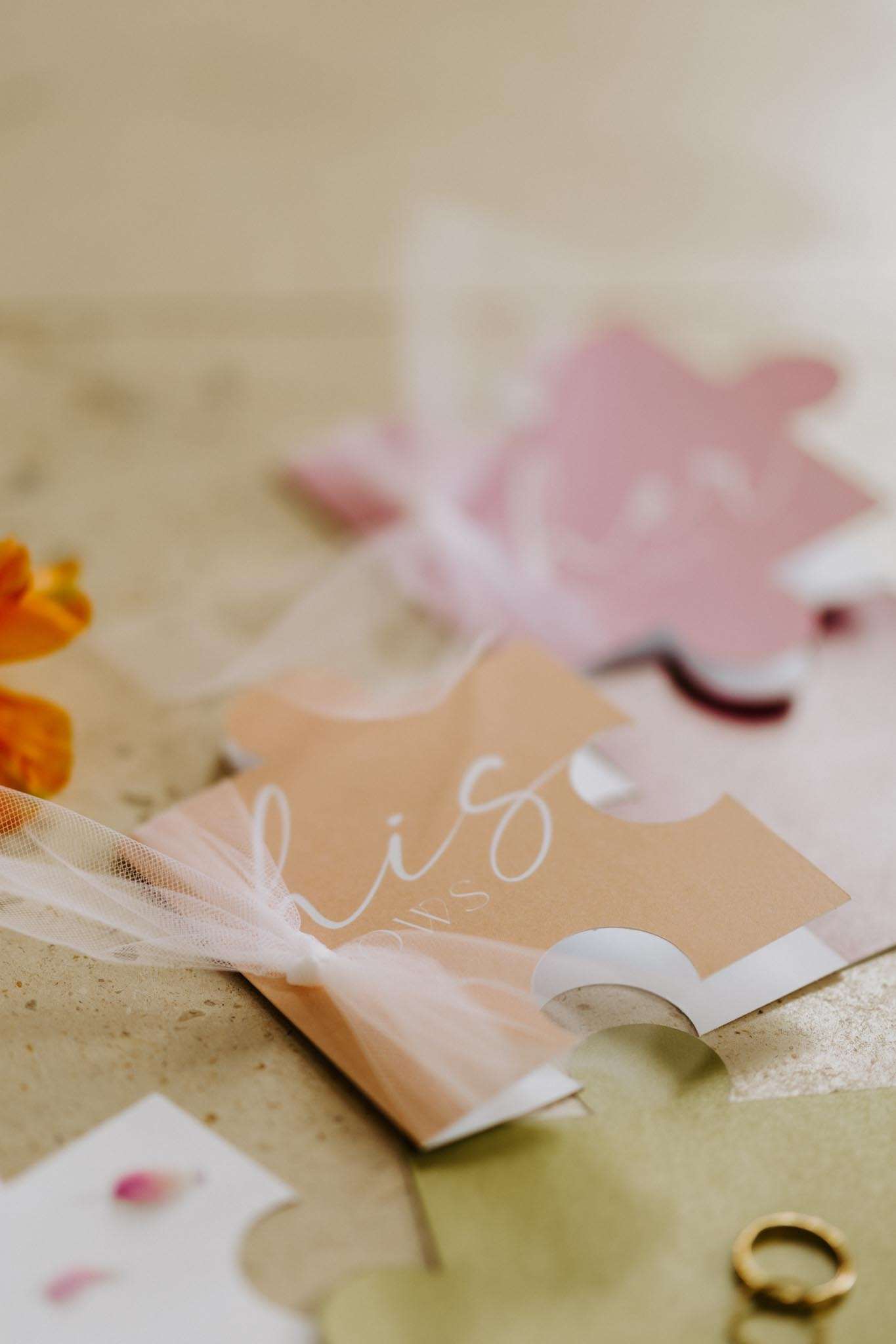 Puzzle-piece place cards in terracotta and dusty rose with white calligraphy and tulle ribbon