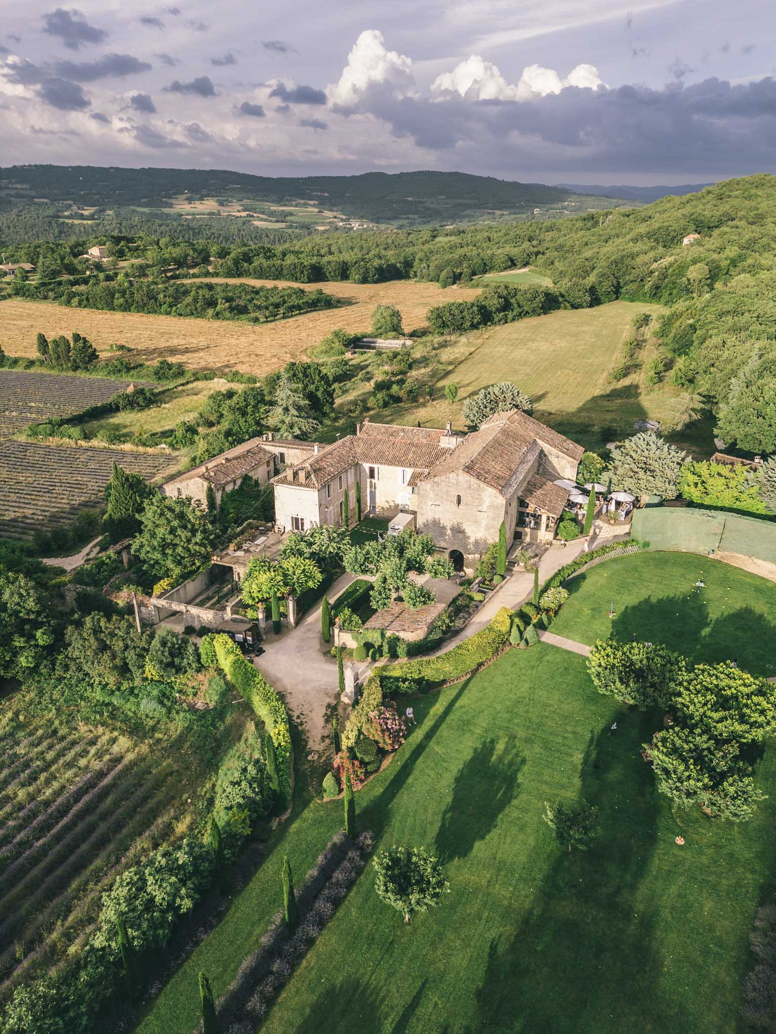 Aerial Provencal stone mas with terracotta roofs cypress trees lavender rows and rolling countryside under cloudy sky