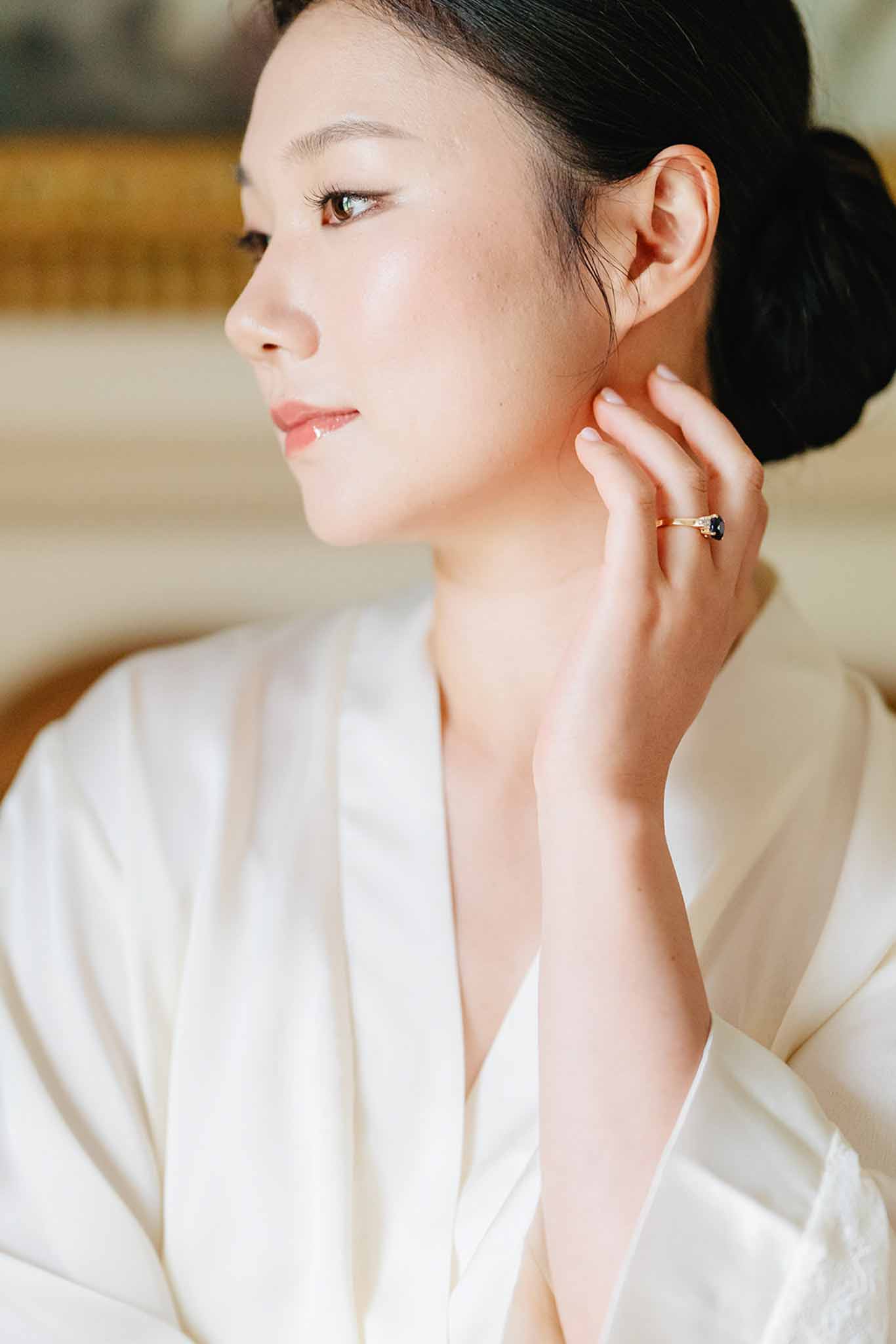 Close-up profile of bride in silk robe showing gold engagement ring during getting ready preparations