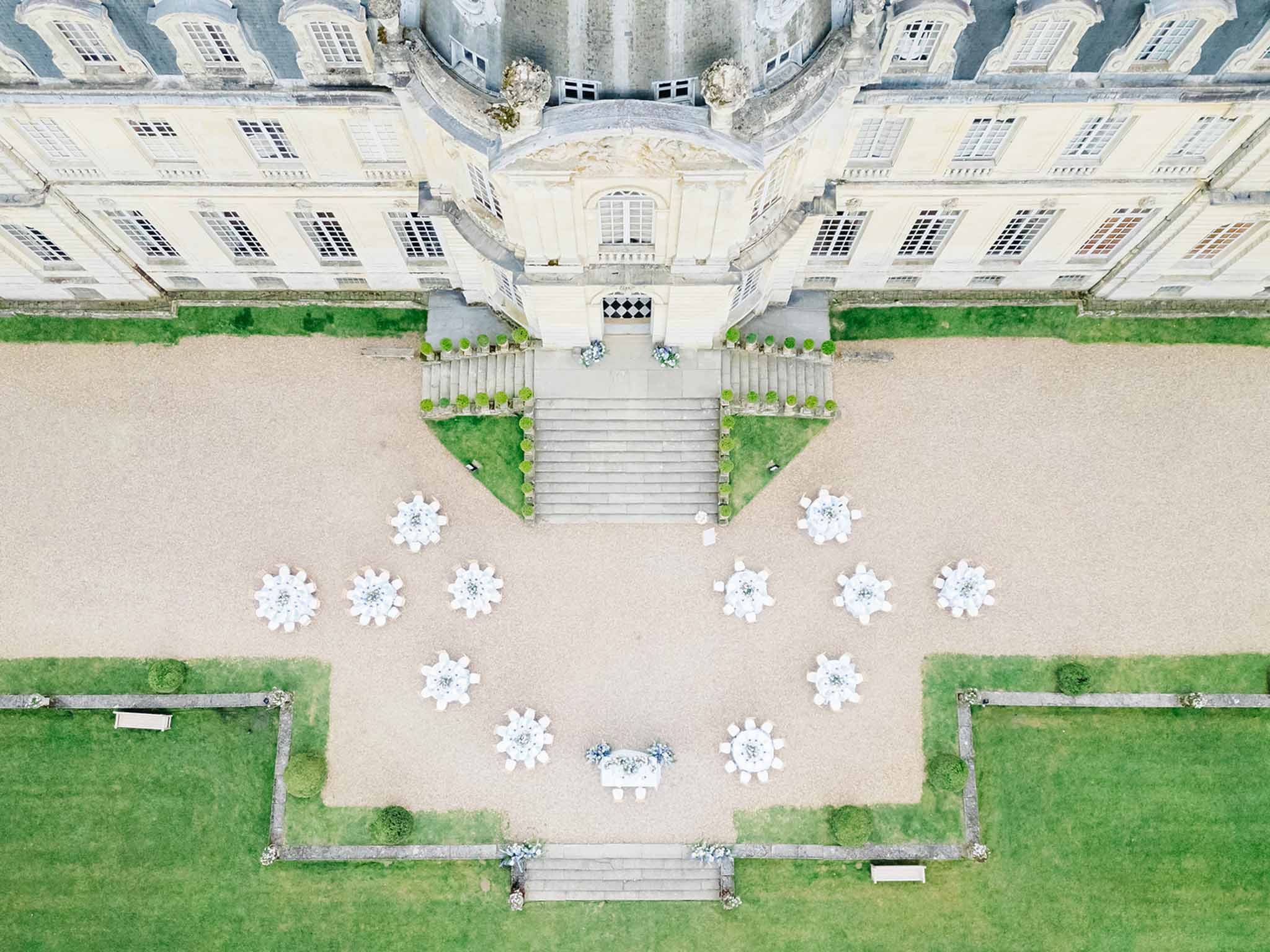 Aerial view of outdoor cocktail reception with round tables on gravel terrace at neoclassical chateau