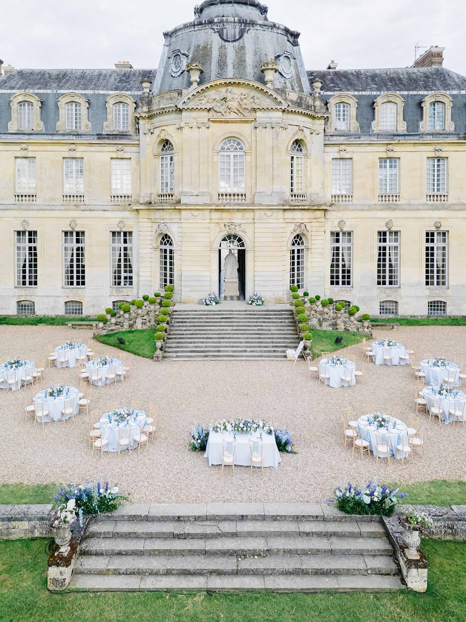 Aerial view of reception with round white tables and blue floral centerpieces in neoclassical chateau courtyard