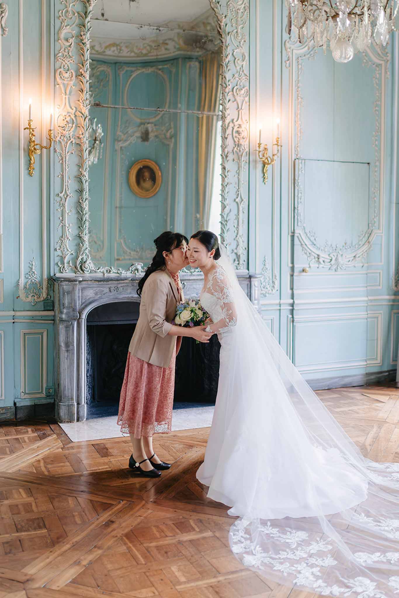 Bride and her mother sharing a kiss on the cheek in an ornate French rococo palace interior
