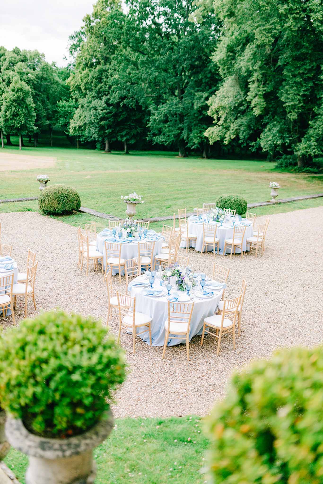 Overhead view of round reception tables with blue linens and white floral centerpieces on gravel courtyard
