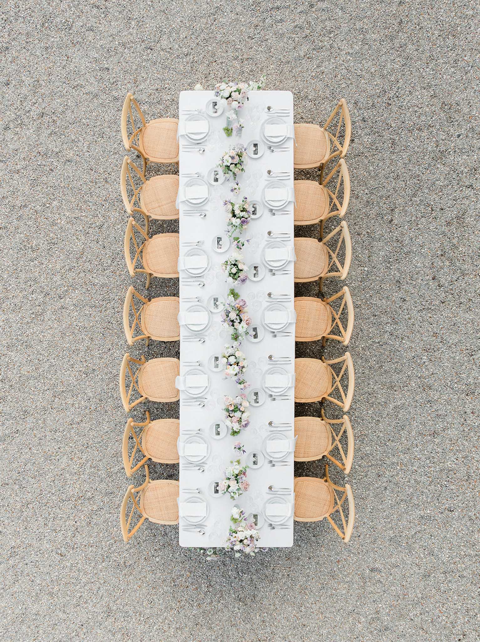 Overhead view of long reception table with white cloth, rattan chairs, and continuous floral runner of white roses and cream peonies