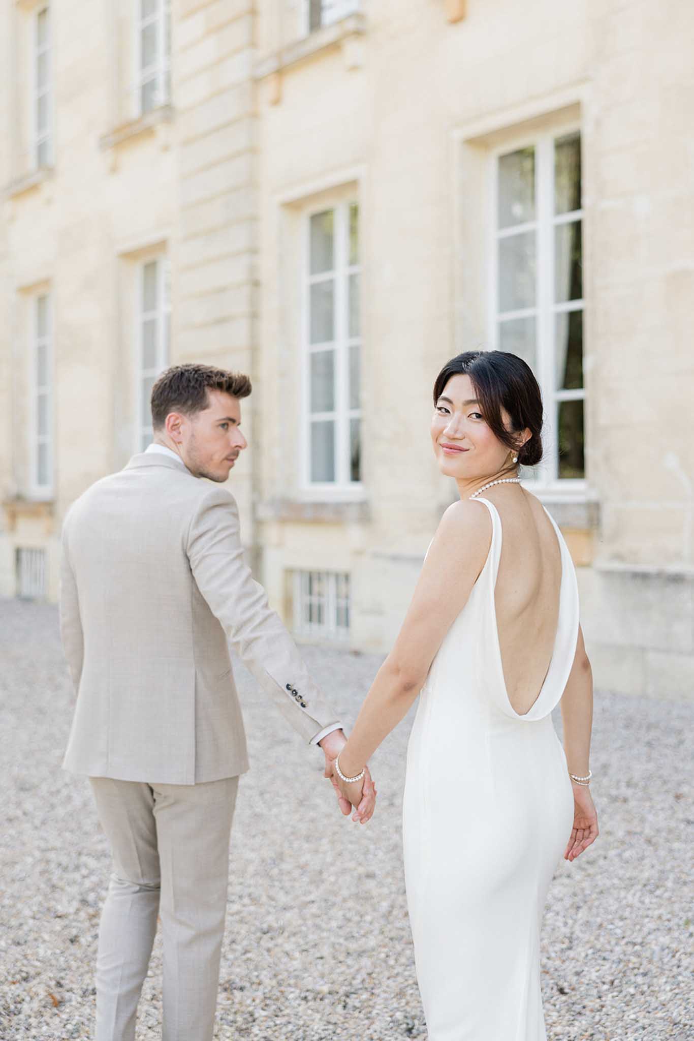 Bride and groom walking hand-in-hand through a classical stone courtyard at Chateau de Courtomer