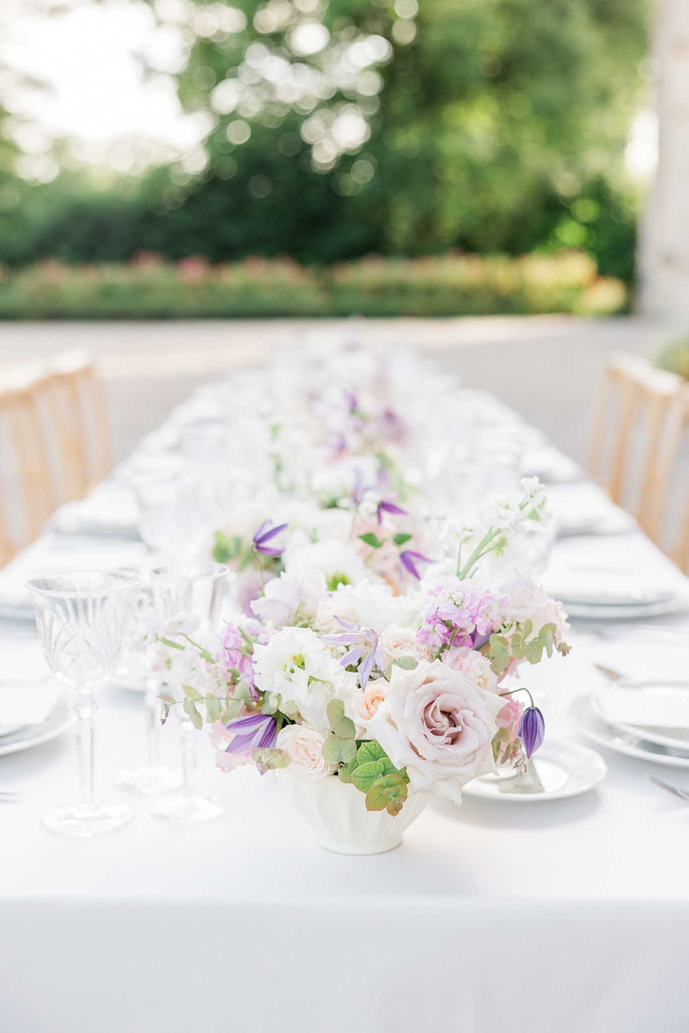 Close-up of outdoor reception centerpiece with dusty mauve roses, purple clematis and white garden roses in a ceramic vase