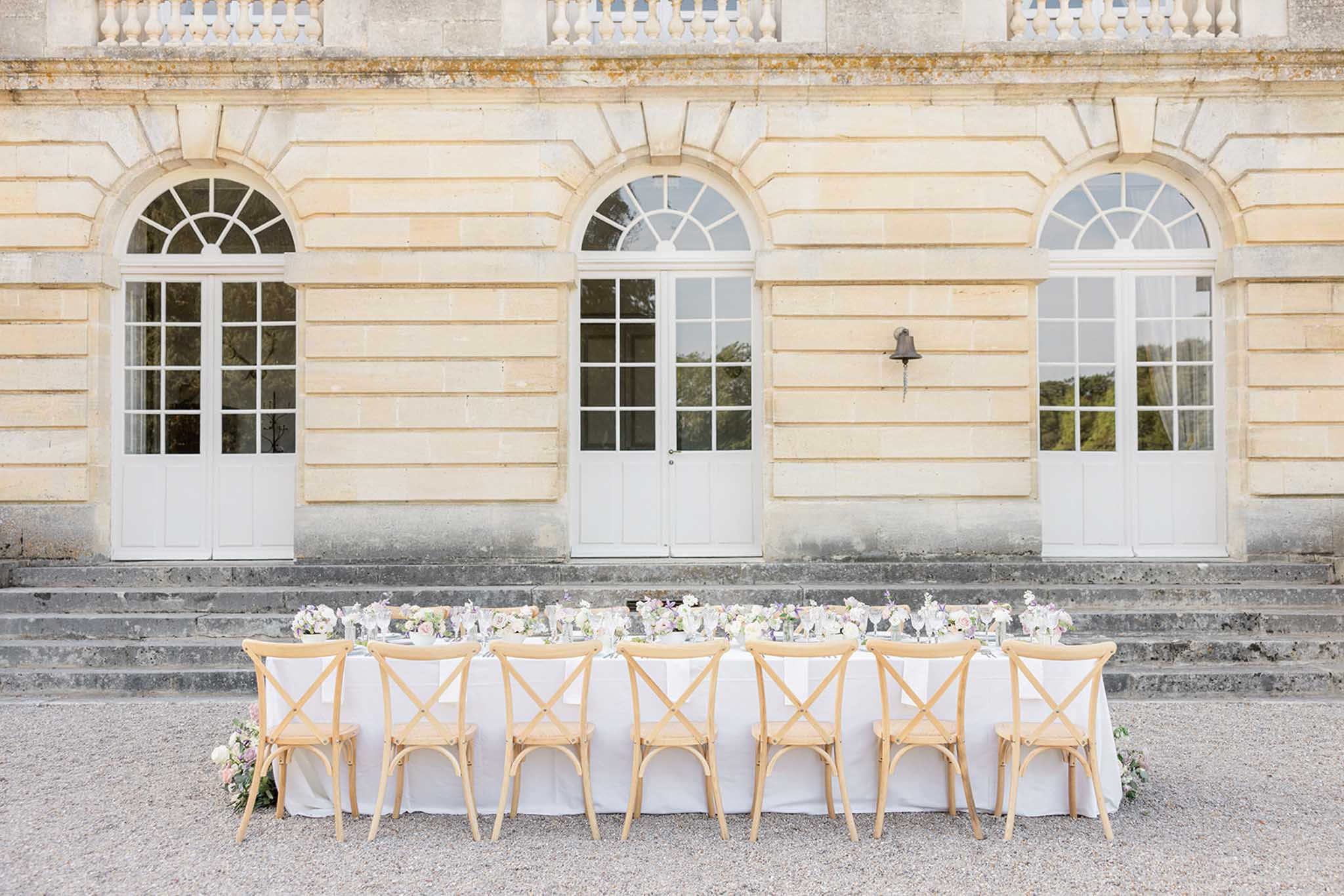 Long outdoor reception table with white linens and floral centerpieces before neoclassical stone building