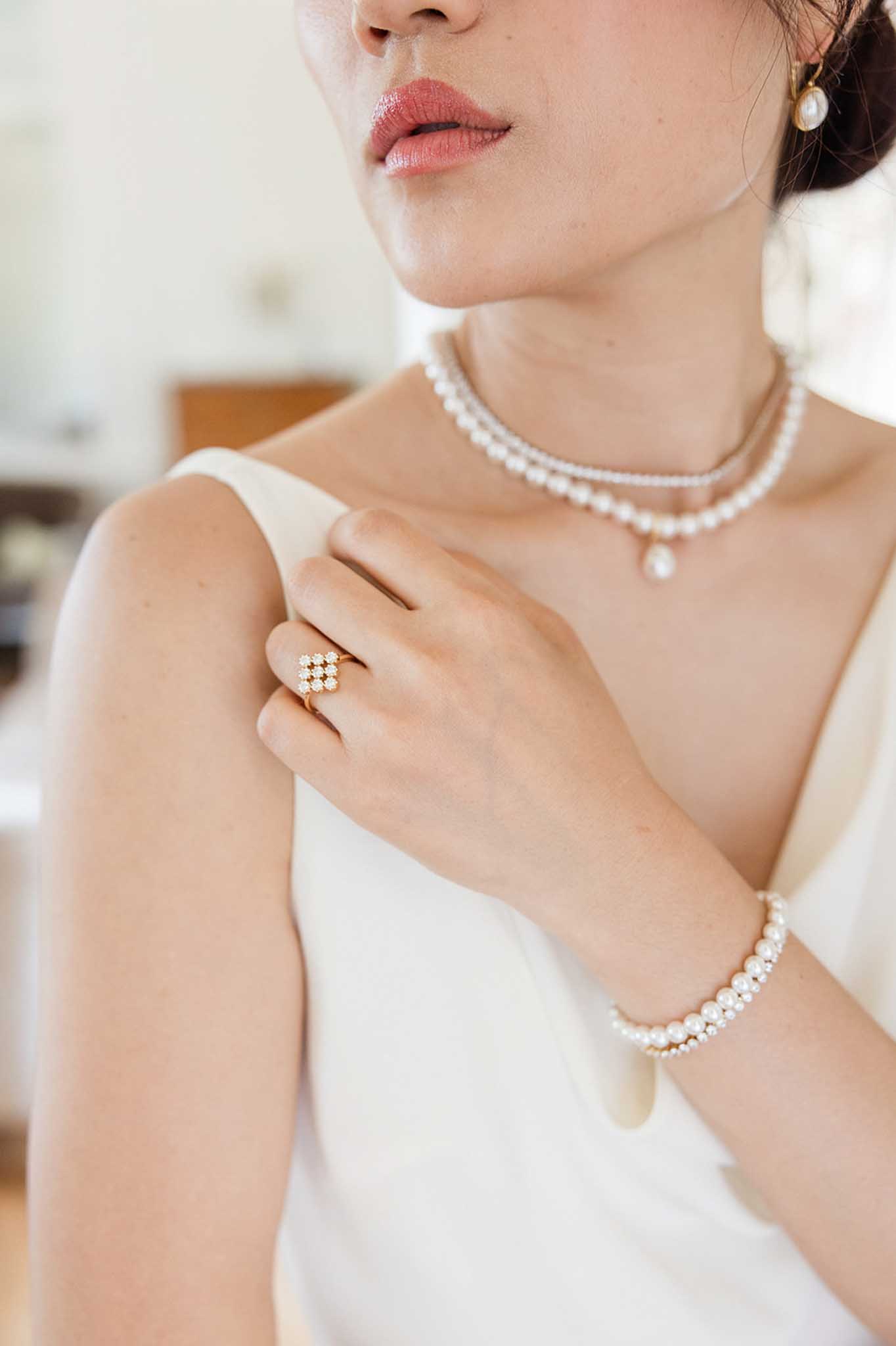 Close-up of bride showing pearl necklace, pearl bracelet, and diamond ring, white sleeveless dress, styled updo