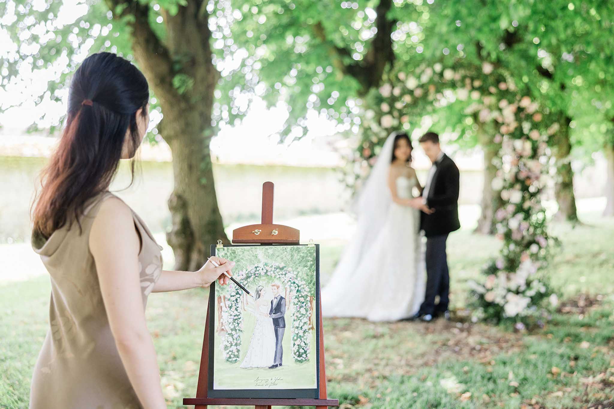 Artist painting live illustration of ceremony while bride and groom exchange vows under floral arbor