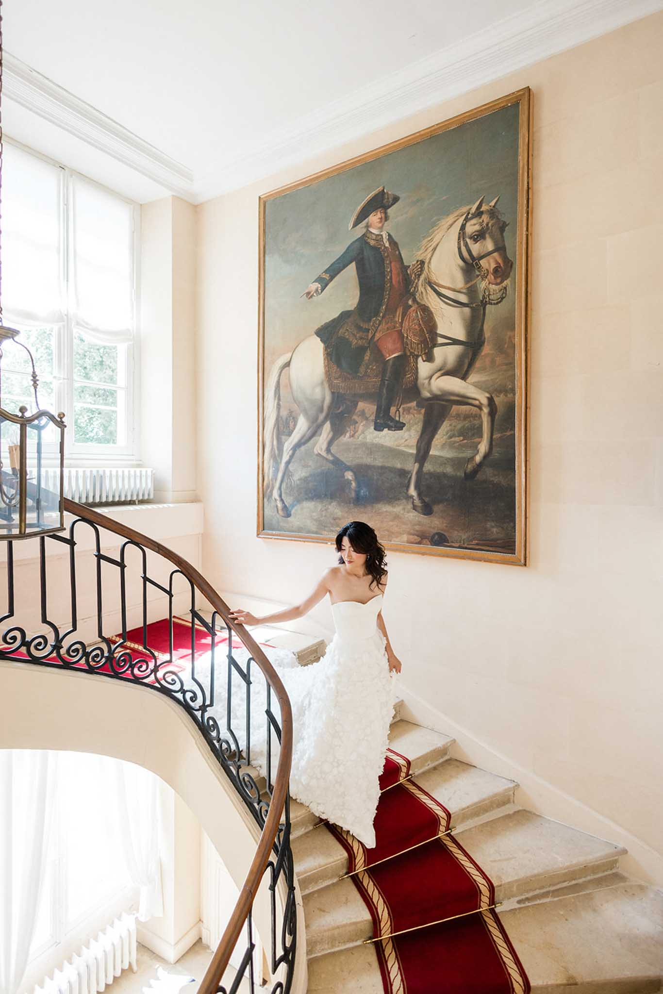 Bride descending grand staircase with wrought-iron banister in classical interior