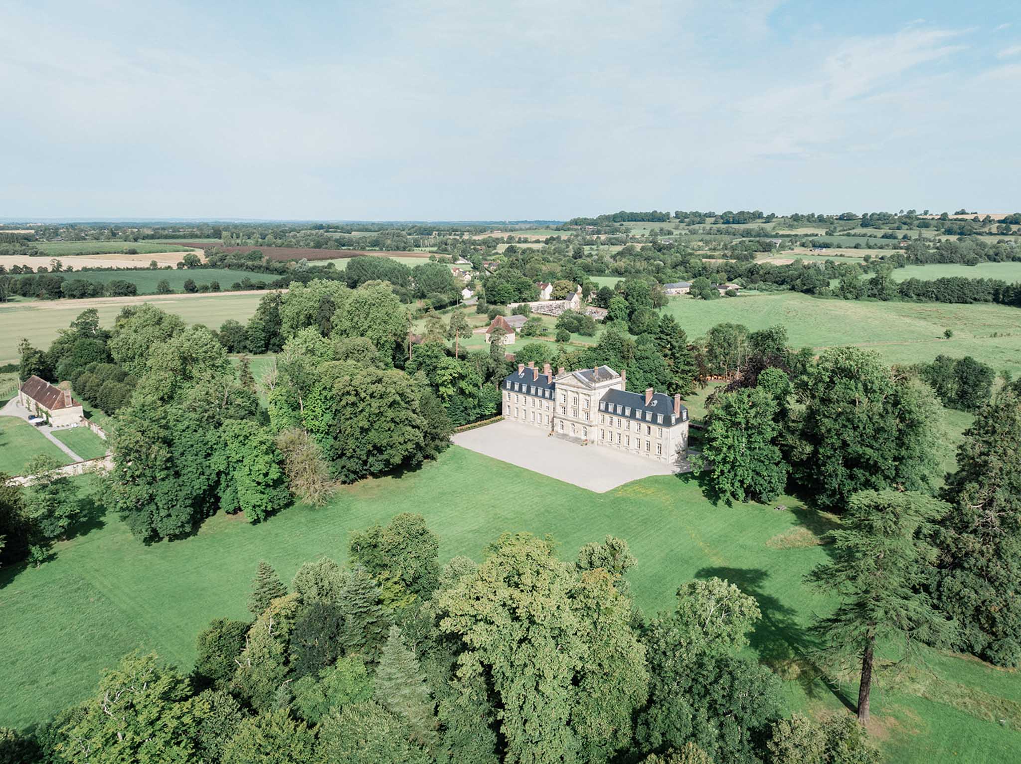 Aerial view of classical French château with mansard roofs, manicured grounds, and surrounding woodland