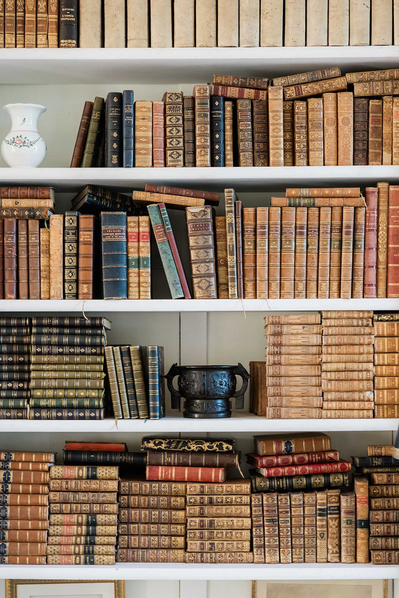 Built-in white shelving filled with vintage leather-bound books in tan, burgundy and navy with gold embossed spines
