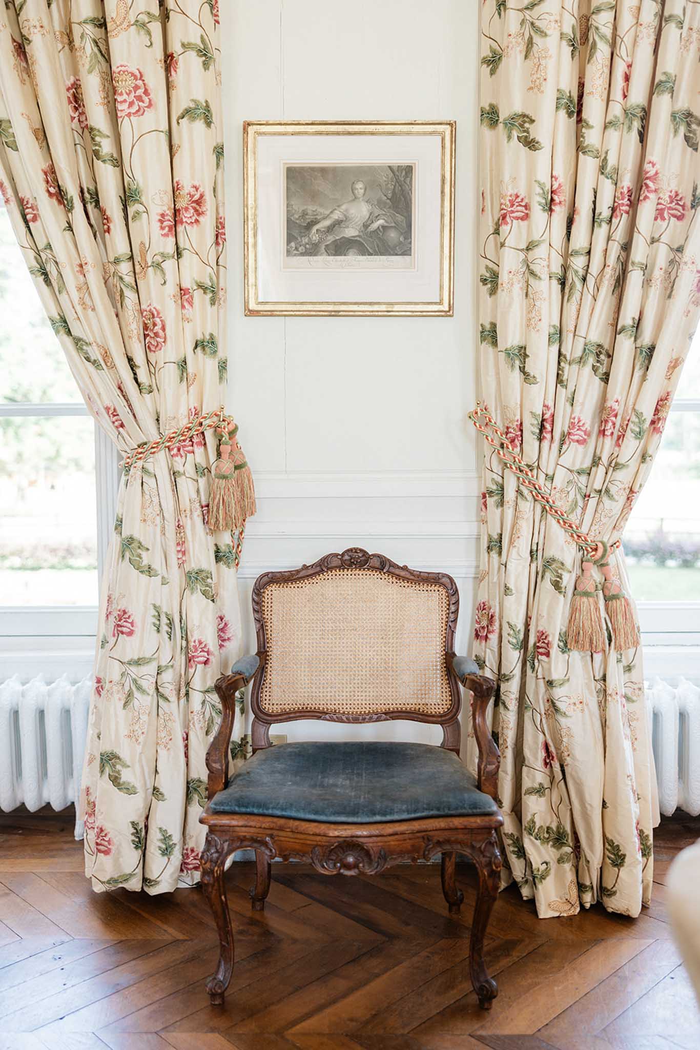 Carved wooden chair with slate-blue velvet seat between floral curtain panels in classical interior getting-ready room