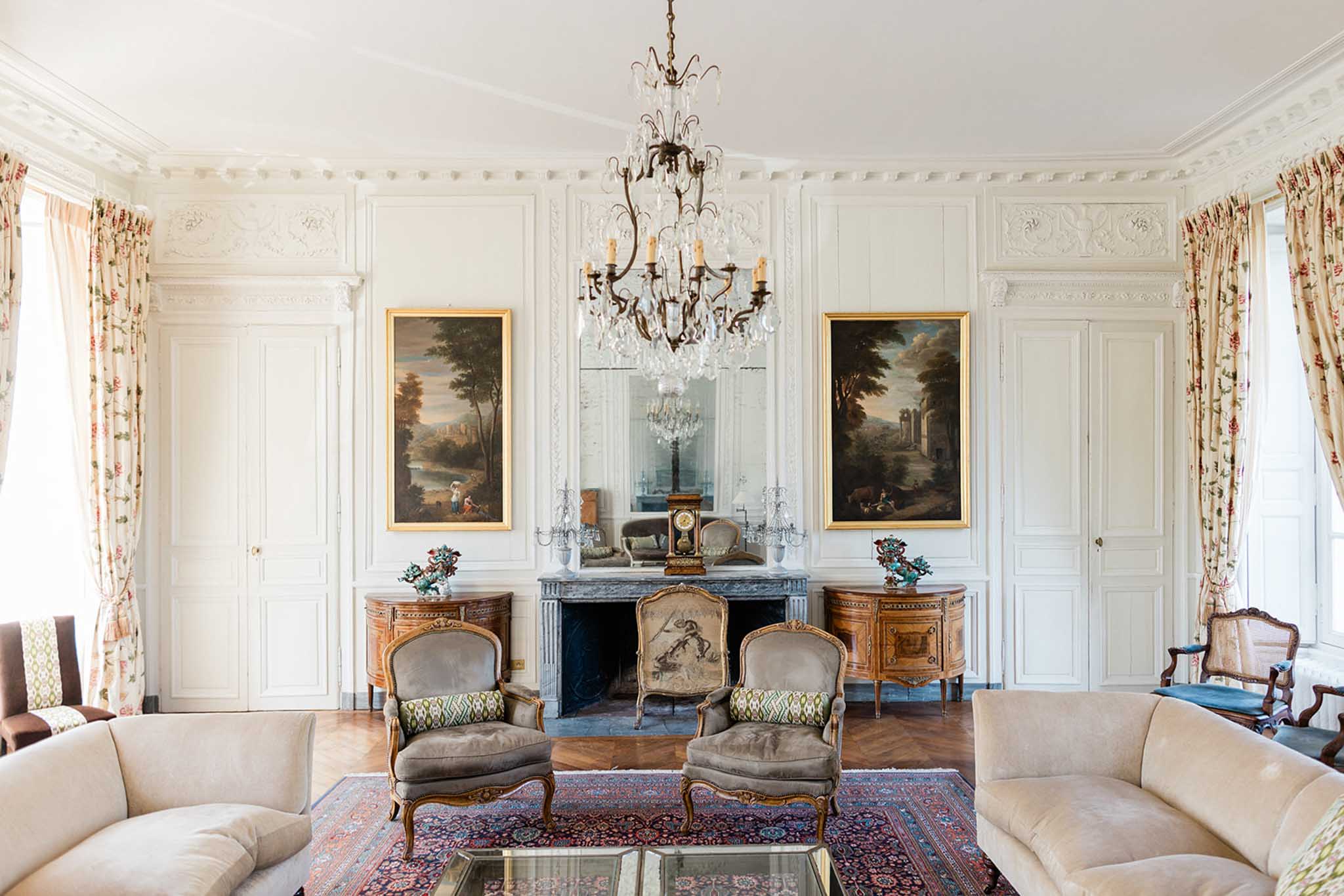 Grand salon interior with crystal chandelier, gold-framed paintings, and classical French furnishings