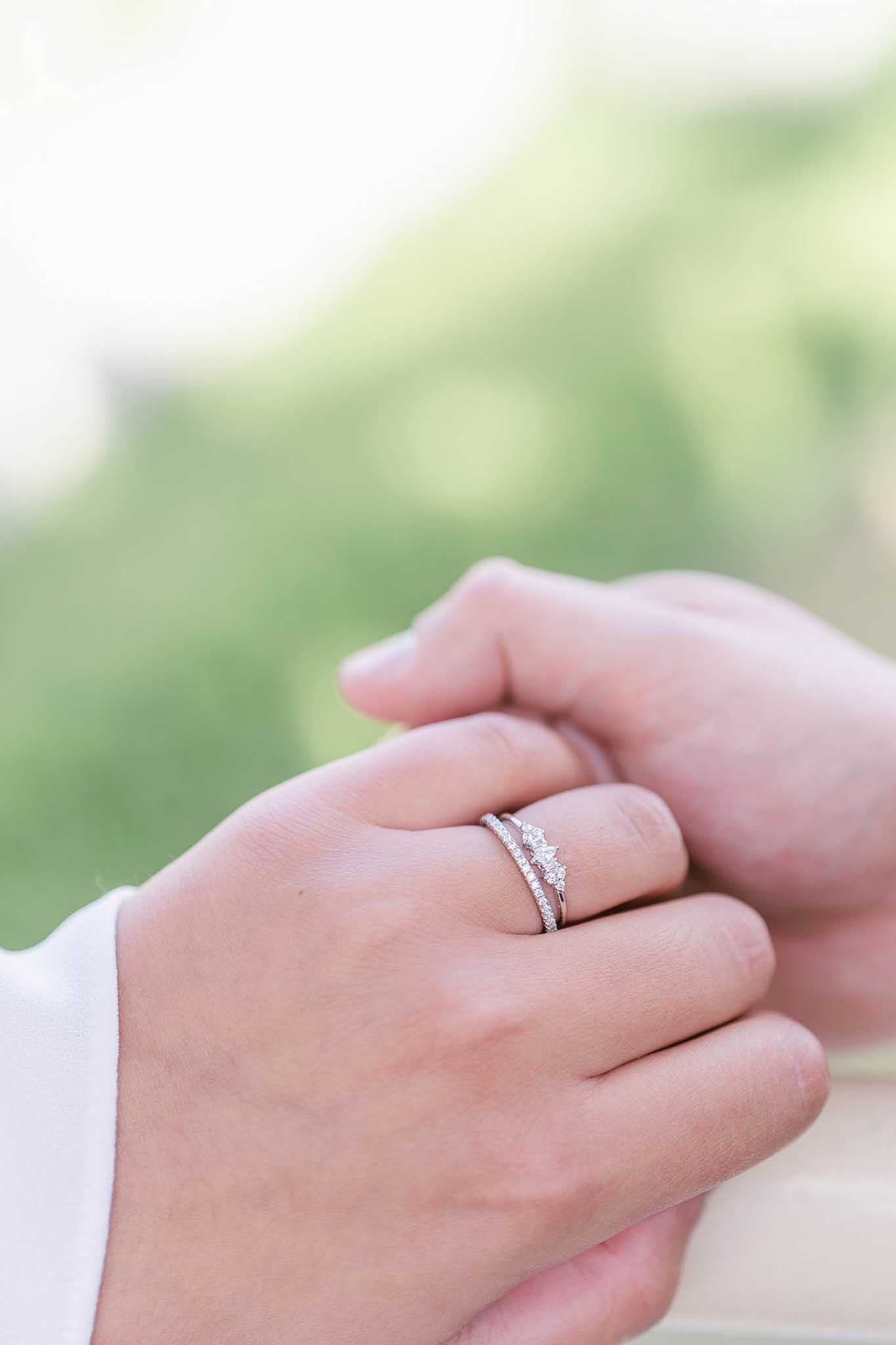 Close-up of bride's wedding ring with diamond chevron setting on groom's hand in garden