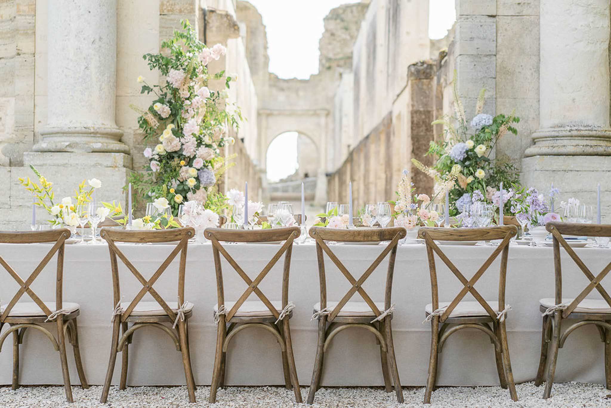 Long banquet table in stone courtyard with tall columns and blush, lavender, and yellow floral centerpieces