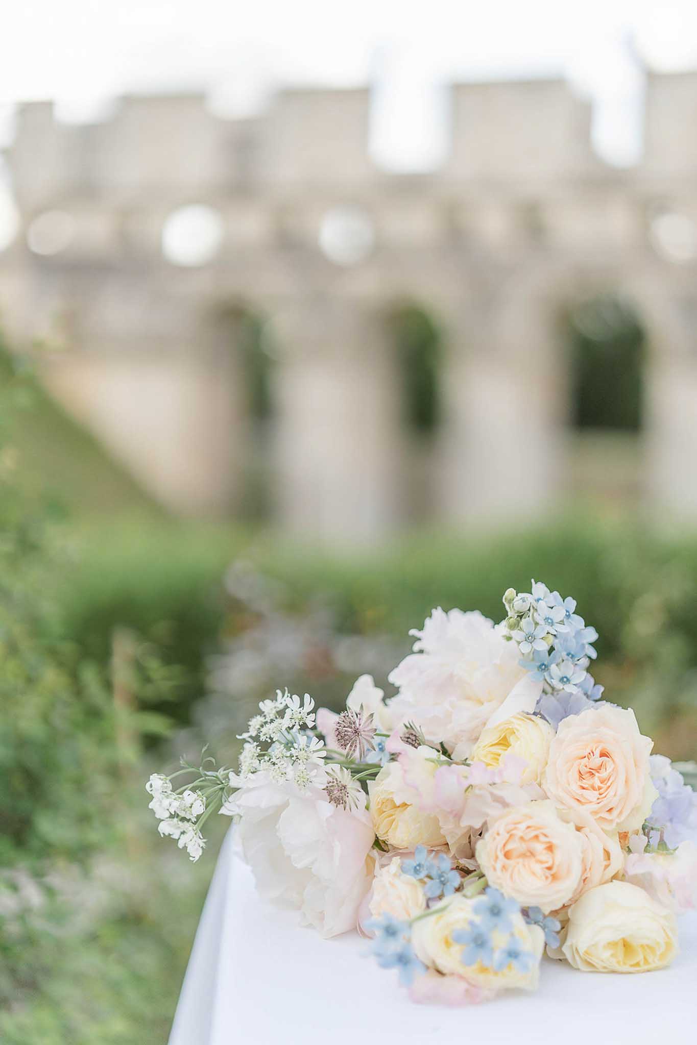 Bridal bouquet with apricot garden roses, white peonies, and blue forget-me-nots on white fabric