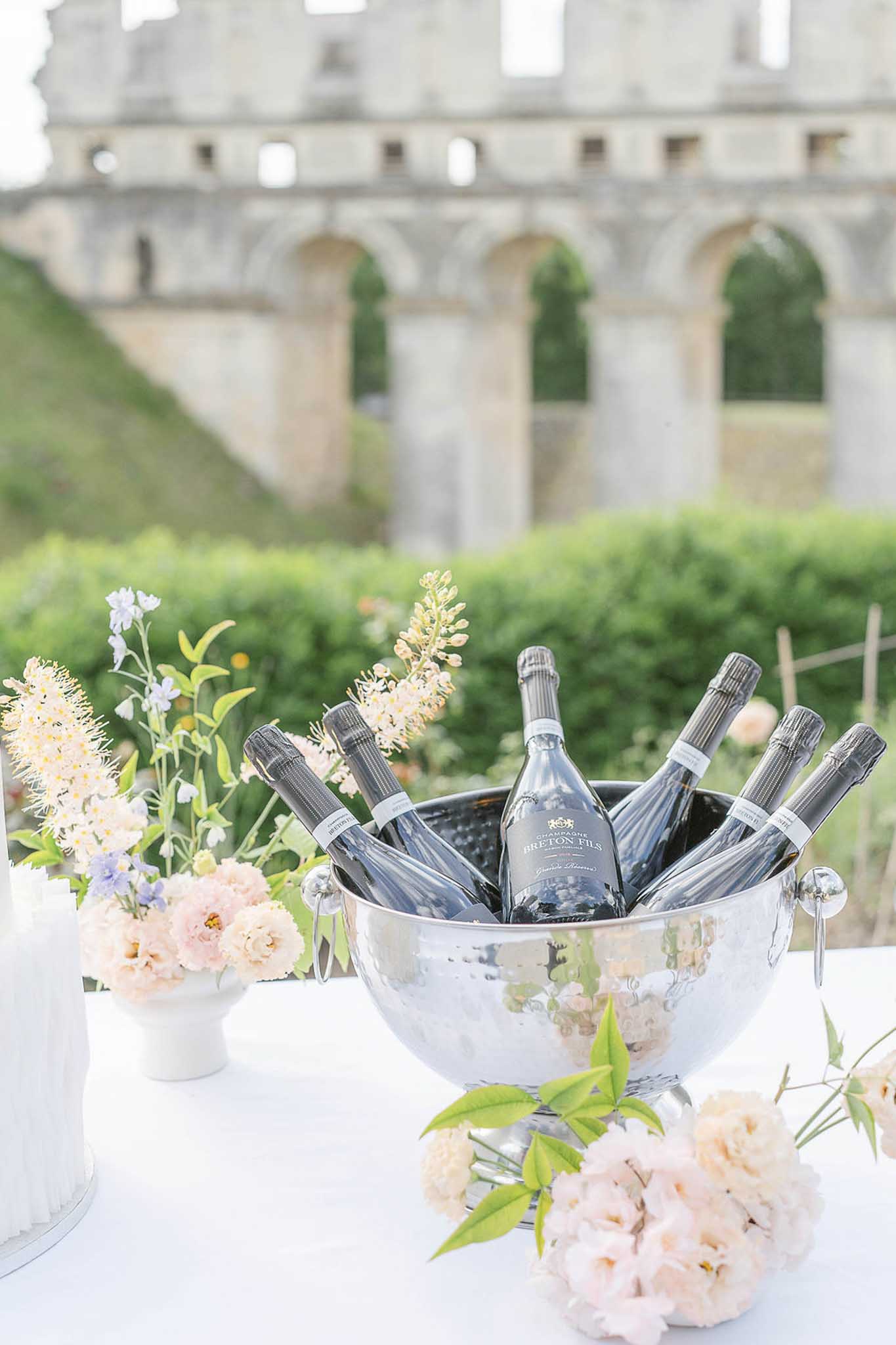 Silver champagne bucket and pink peony arrangements on white-draped table at outdoor cocktail reception