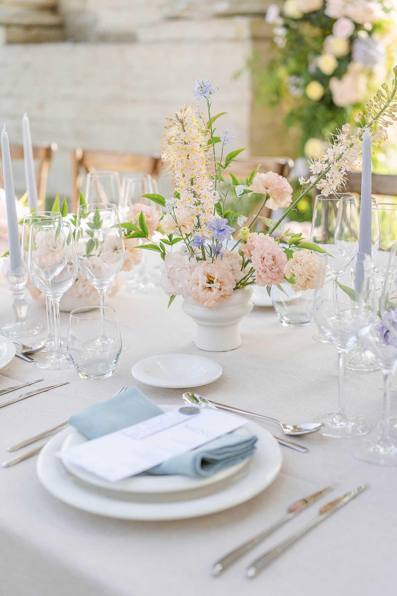 Reception centerpiece with blush roses, yellow astilbe, and blue delphinium with pastel place settings