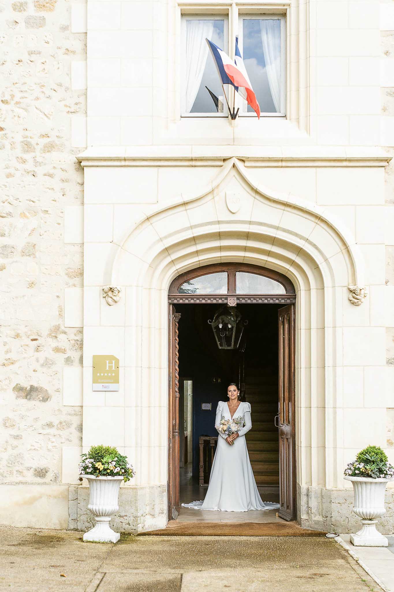Bride standing in grand arched doorway of classical stone building holding bouquet