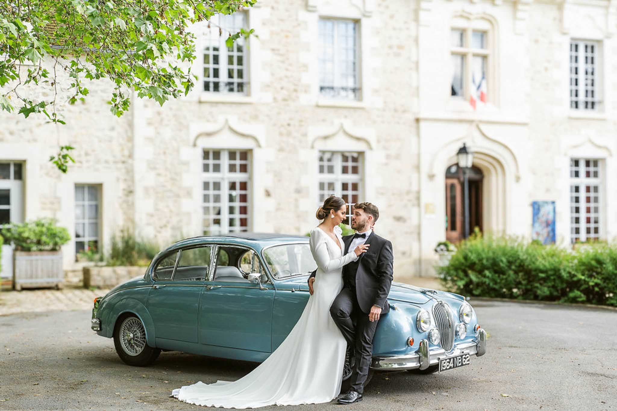 Bride and groom beside vintage teal and blue two-tone car in courtyard of classical stone manor house