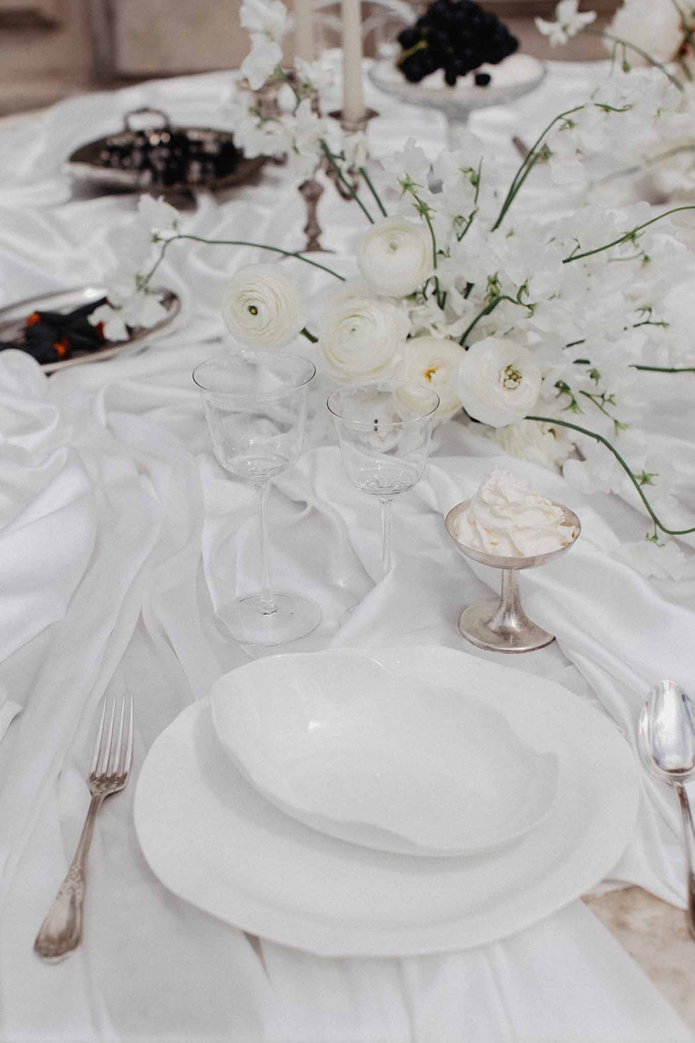 Reception table setting with cream ranunculus and baby's breath centerpiece beside silver flatware