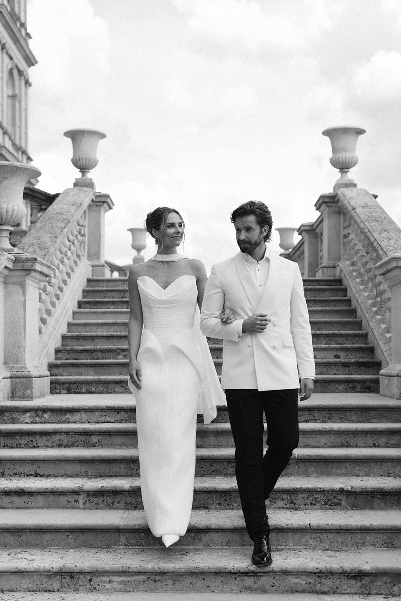 Black and white portrait of couple descending grand stone staircase with ornamental urns and balustrades