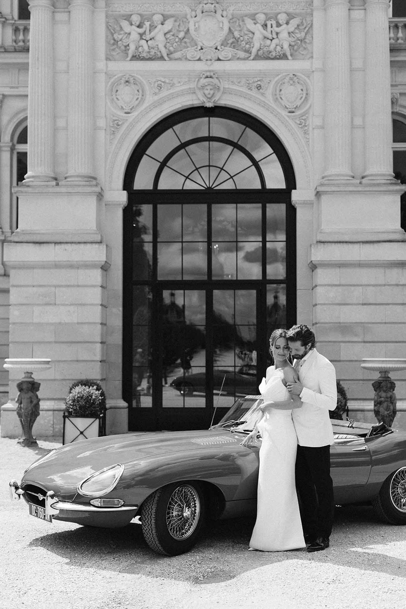 Bride and groom posing beside a vintage car at their wedding
