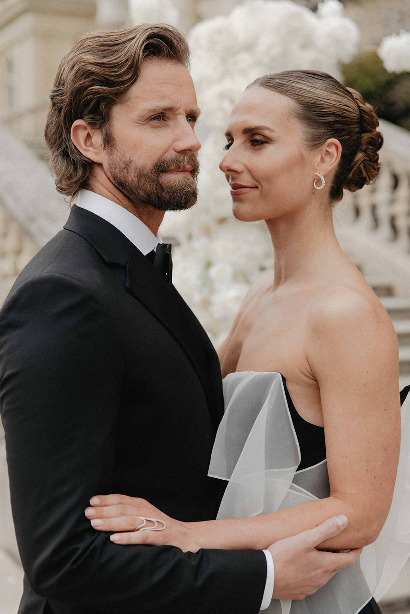 Bride in black gown with white tulle overlay and groom in tuxedo against white florals