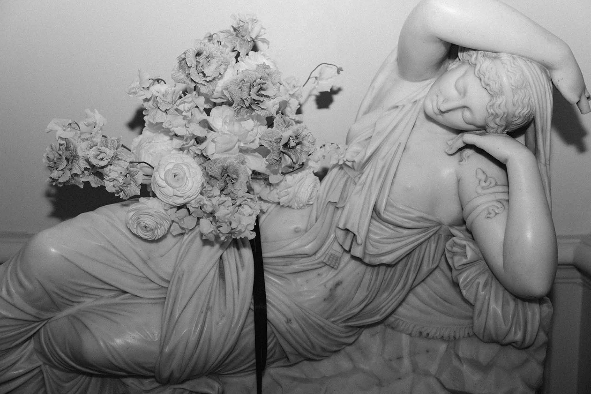 Black-and-white bride reclining holding bouquet of ranunculus and peonies