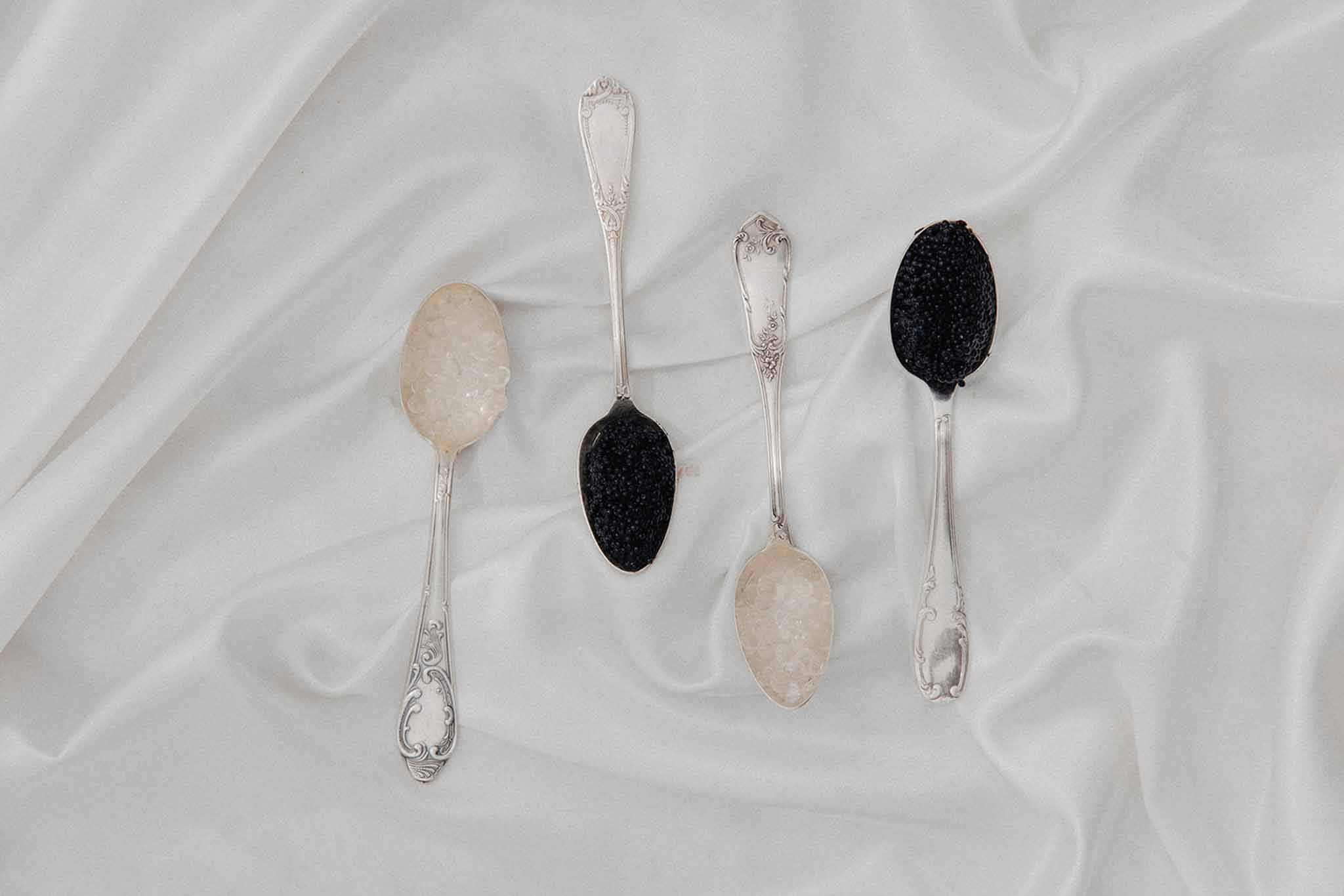 Four vintage silver spoons with cream and black textured bowls arranged on white linen