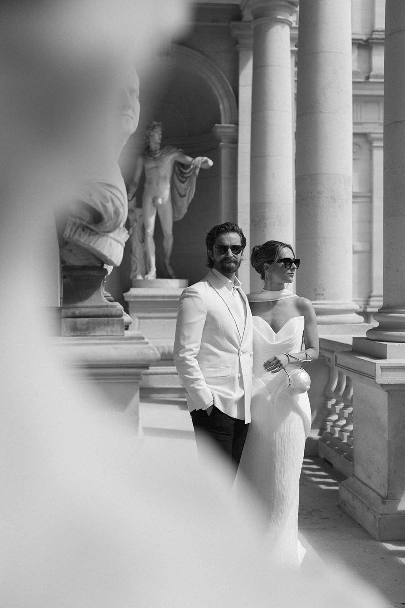 Couple walking arm-in-arm through Corinthian colonnade in black and white at Chateau de Ferrieres