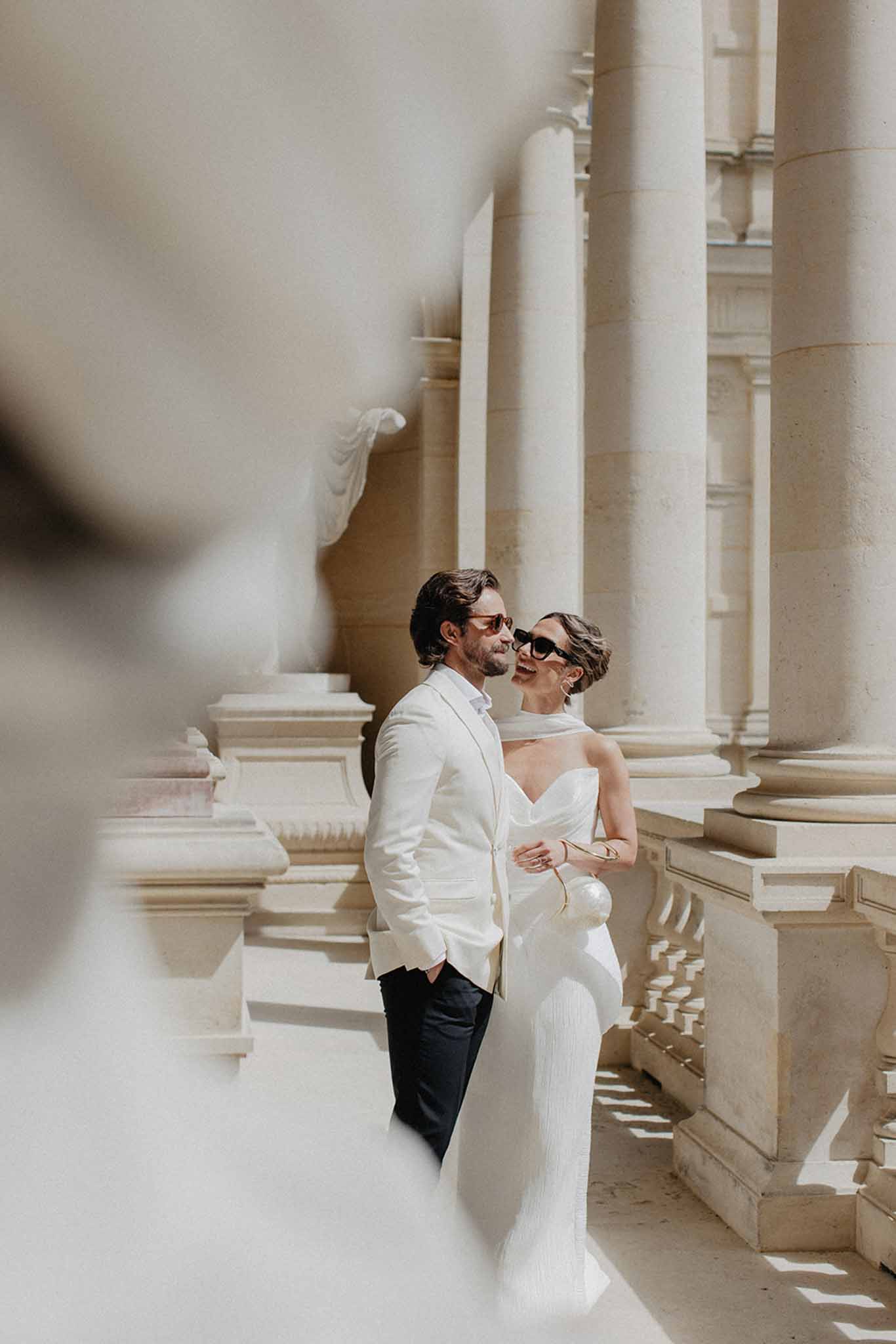 Bride and groom in sunglasses walking through neoclassical colonnade at Chateau de Ferrieres