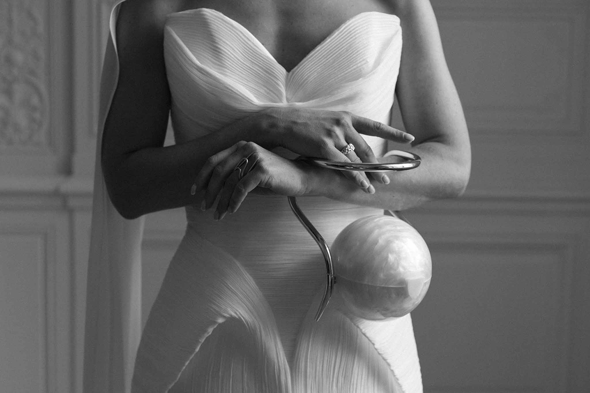 Black-and-white close-up of bride in pleated sweetheart gown holding stethoscope, engagement ring visible on left hand