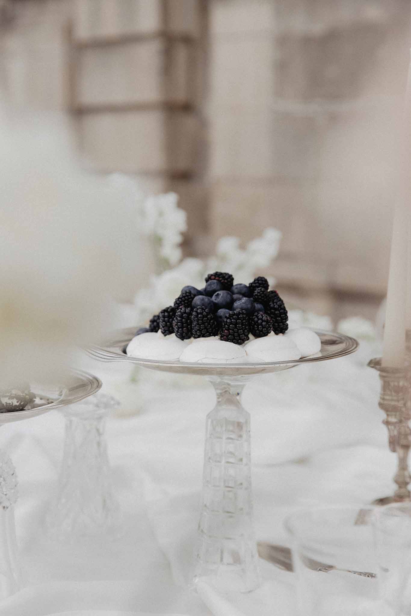 White meringue dessert topped with fresh blackberries and blueberries on glass pedestal cake stand