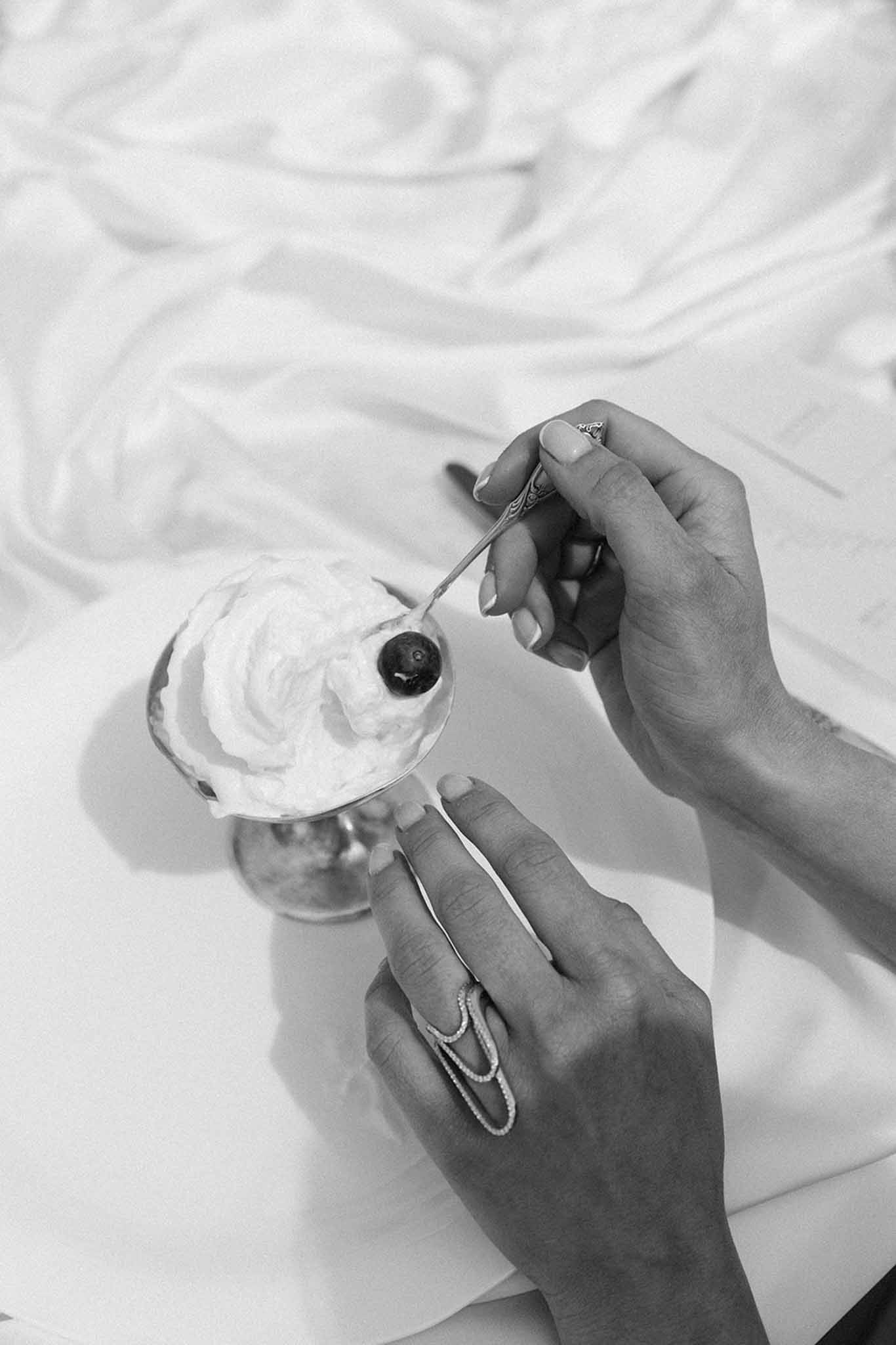 Black and white overhead detail of bride's hands holding a small spoon and a white plate of dessert during the reception.
