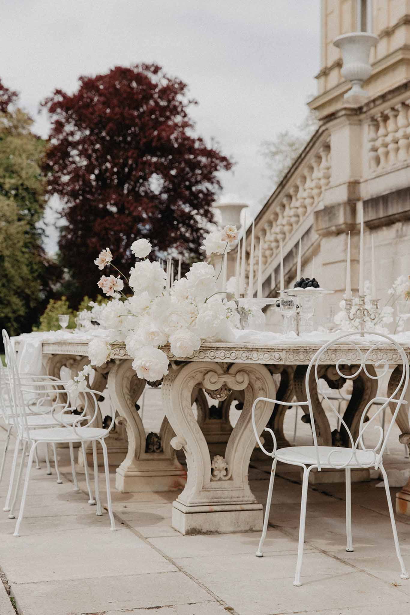 Stone terrace table with ivory and blush peony centerpiece and white bistro chairs at Chateau de Ferrieres