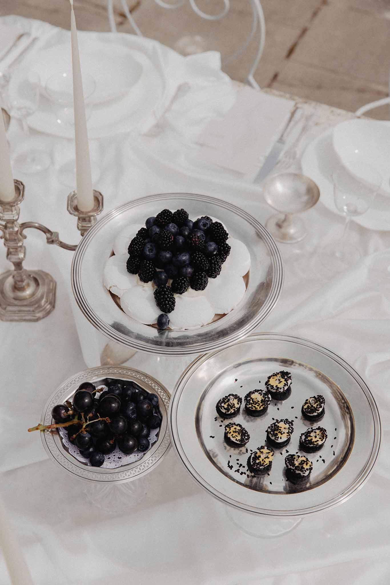 Dessert display with berry pavlova, chocolate tartlets with gold leaf, and grapes in glass bowls