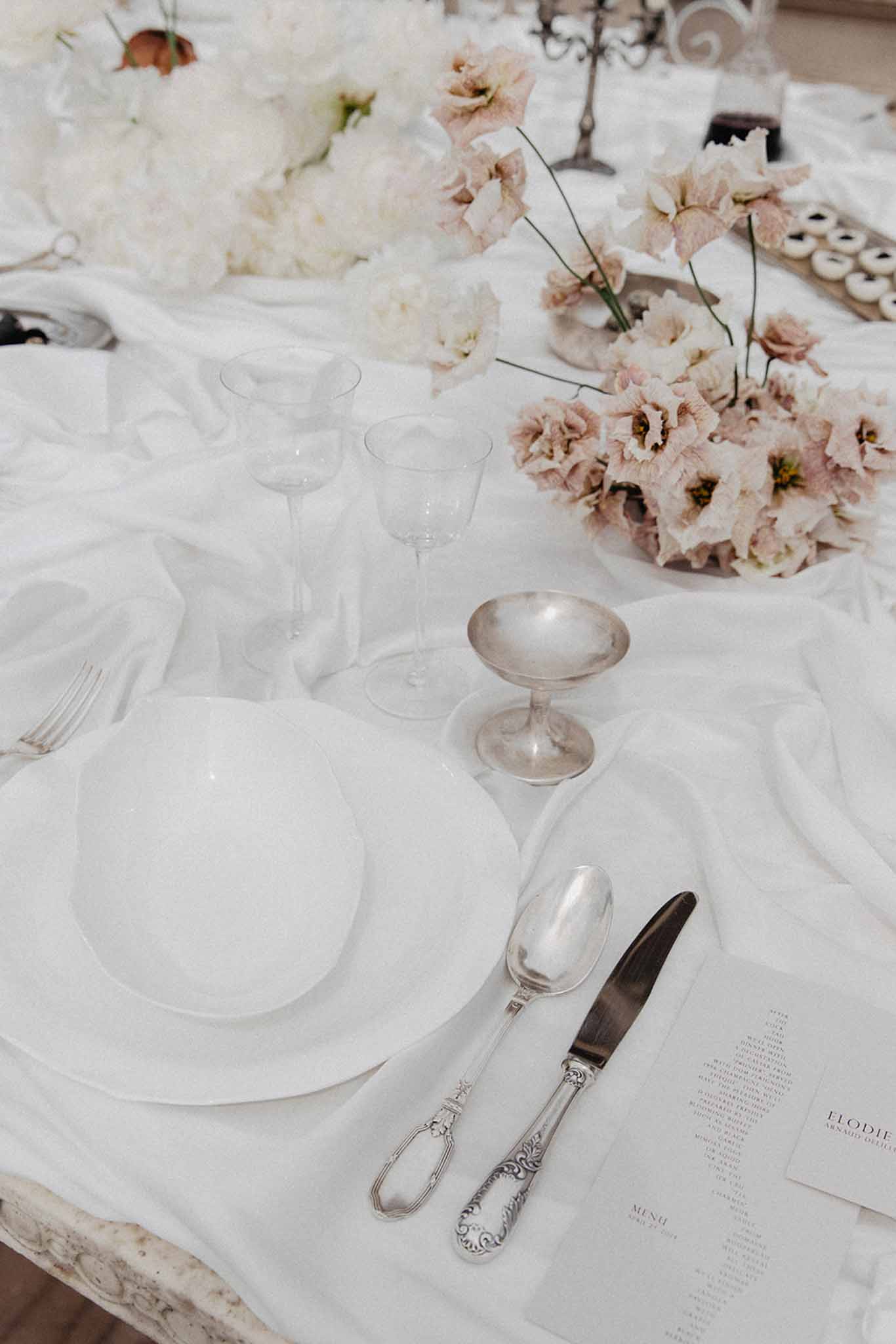 Reception table close-up with coupe glasses, ornate silver flatware, and white linens
