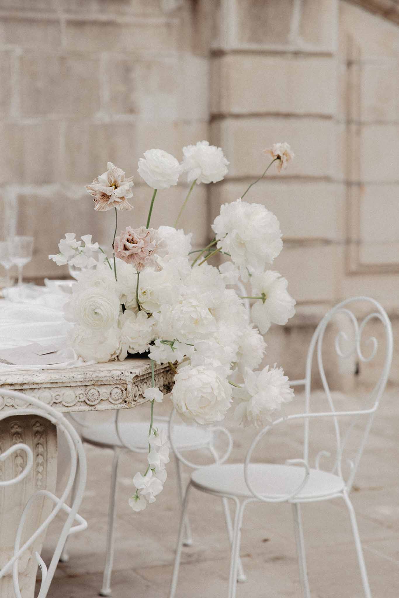 Bridal bouquet of white ranunculus, peonies and blush carnations displayed on ornate cream table