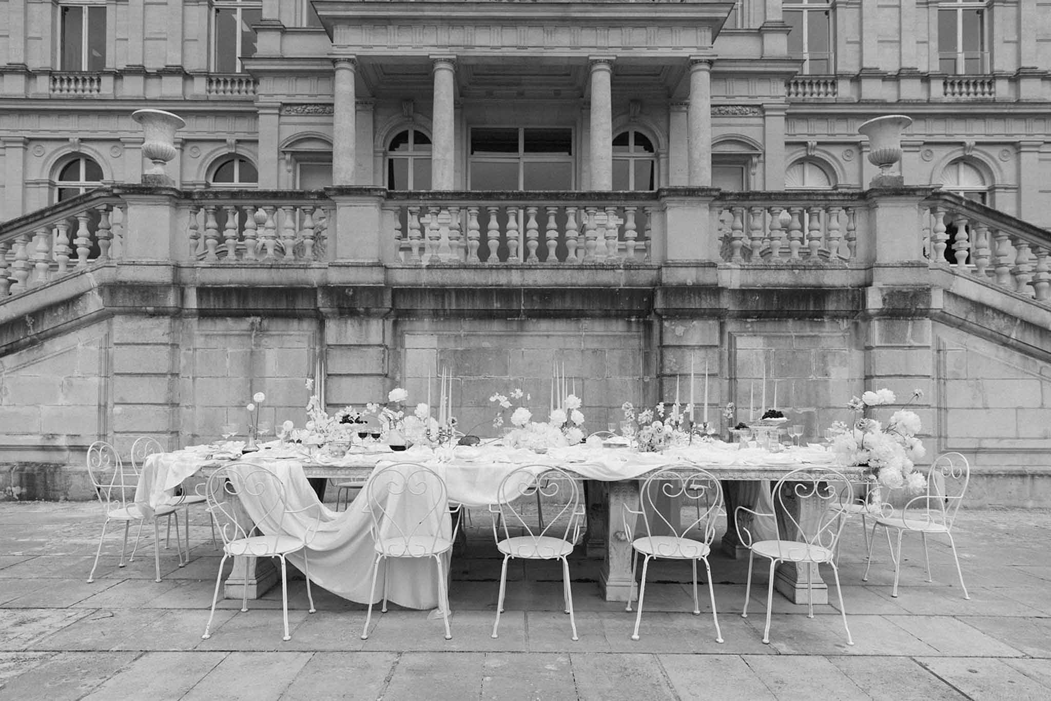 Black and white photo of reception table with heart-backed chairs in neoclassical courtyard